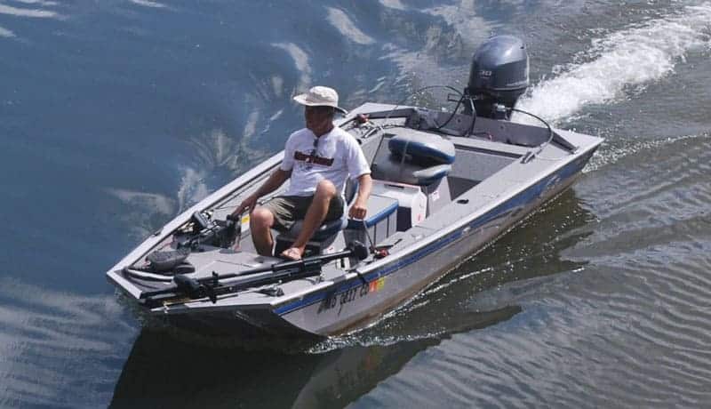Fisherman driving a gray and blue bass boat on the lake.