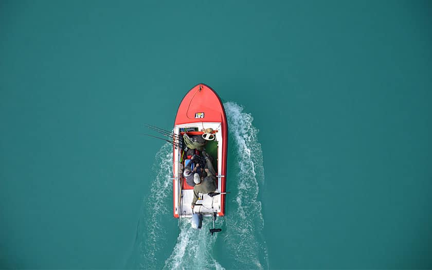Two fishermen driving in a red bass boat on the lake.
